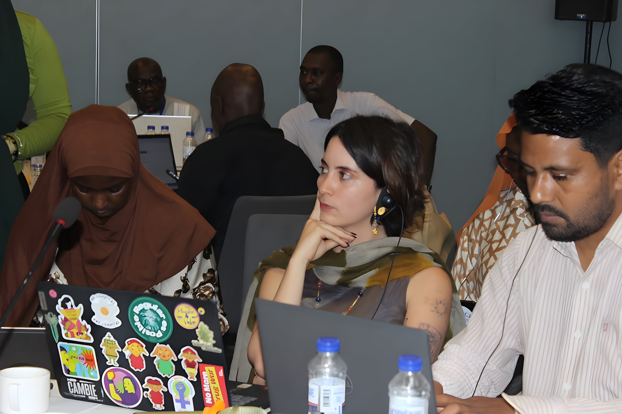 Grande salle de conférence plénière moderne et lumineuse à Dakar, remplie de délégués internationaux attentifs portant des casques de traduction simultanée. À la tribune, des officiels se serrent la main chaleureusement. Les cabines d'interprétation ISO de Translab sont visibles en arrière-plan.